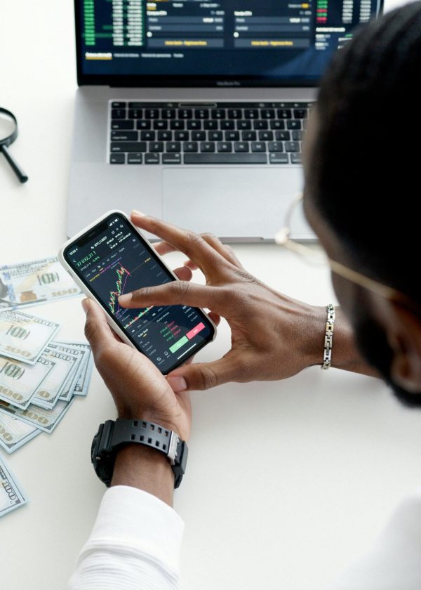pexels-photo-6801872-6801872 A person trading stocks using a smartphone, showcasing financial data on mobile and laptop screens.